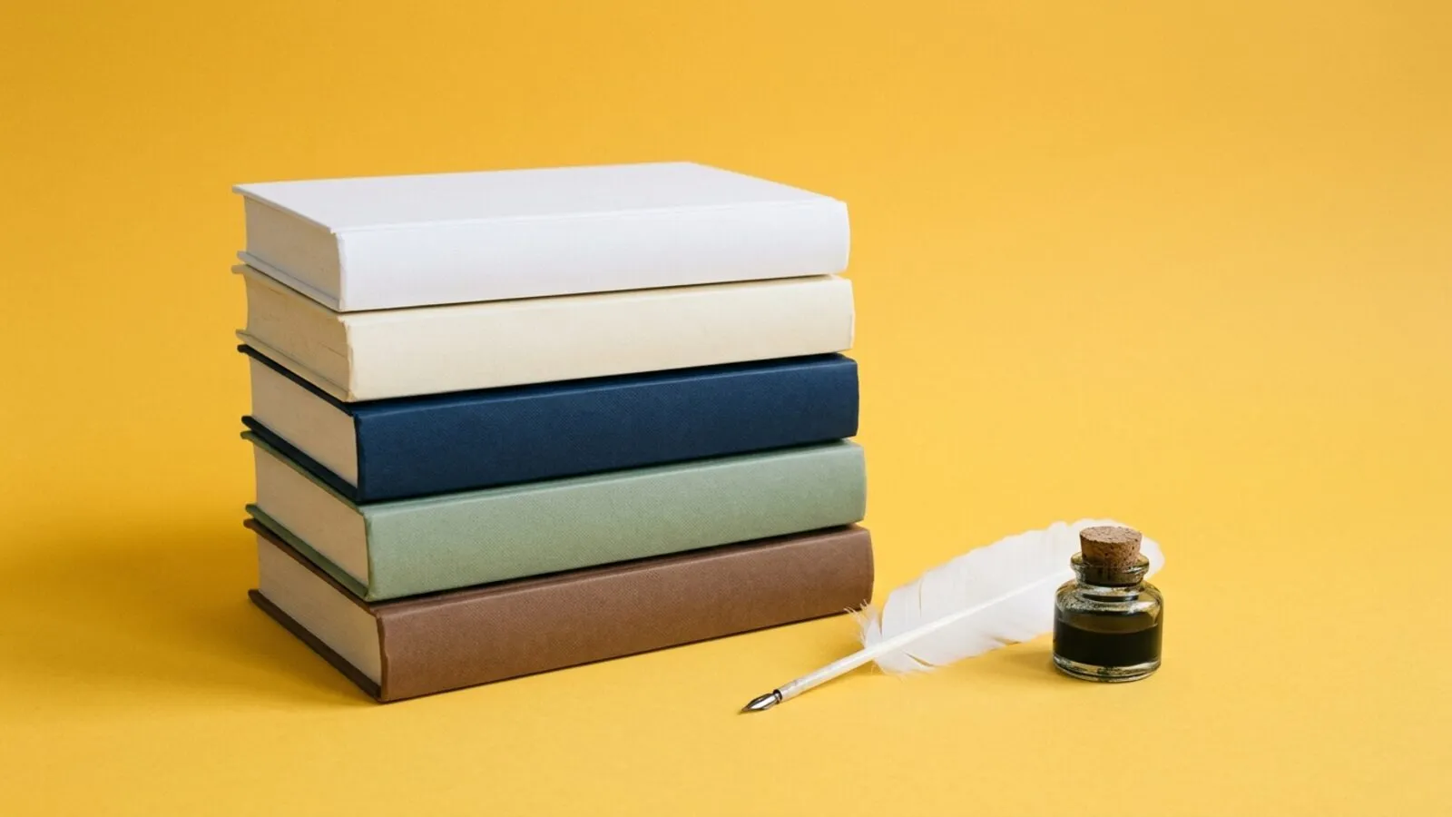 Pile de cinq livres reliés crème, blanc, bleu marine, vert sauge et brun, plume blanche et encrier sur fond jaune