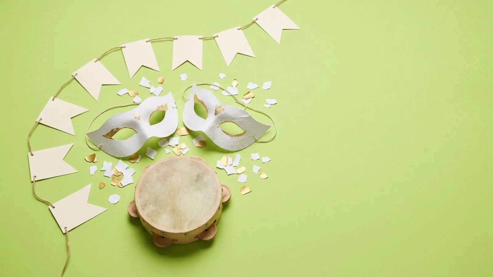 Masques de carnaval blanc et or, confettis, tambourin en bois et guirlande de fanions crème sur fond vert tendre