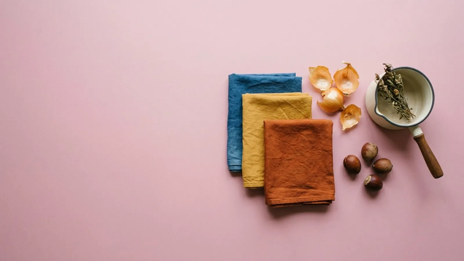 Tissus teints à l'indigo, à l'ocre et à la rouille, pelures d'oignon, noyaux et casserole émaillée sur fond rose