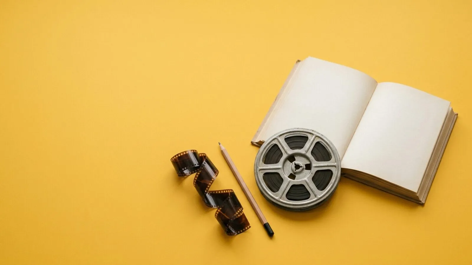 Livre ouvert aux pages crème, bobine de film, bande de pellicule et crayon posés sur fond jaune