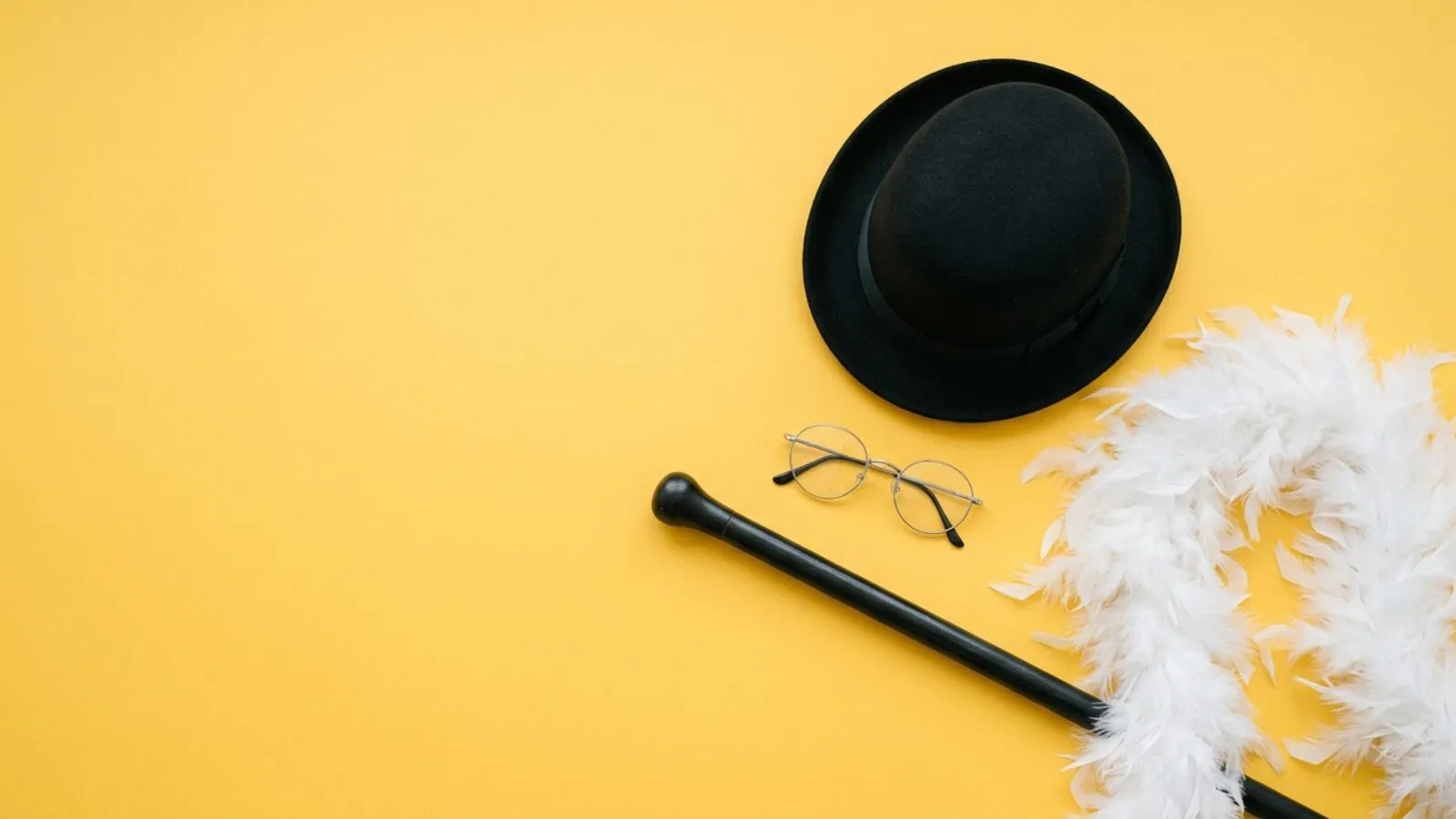 Chapeau melon noir, lunettes rondes cerclées de métal, canne noire et boa de plumes blanches sur fond jaune